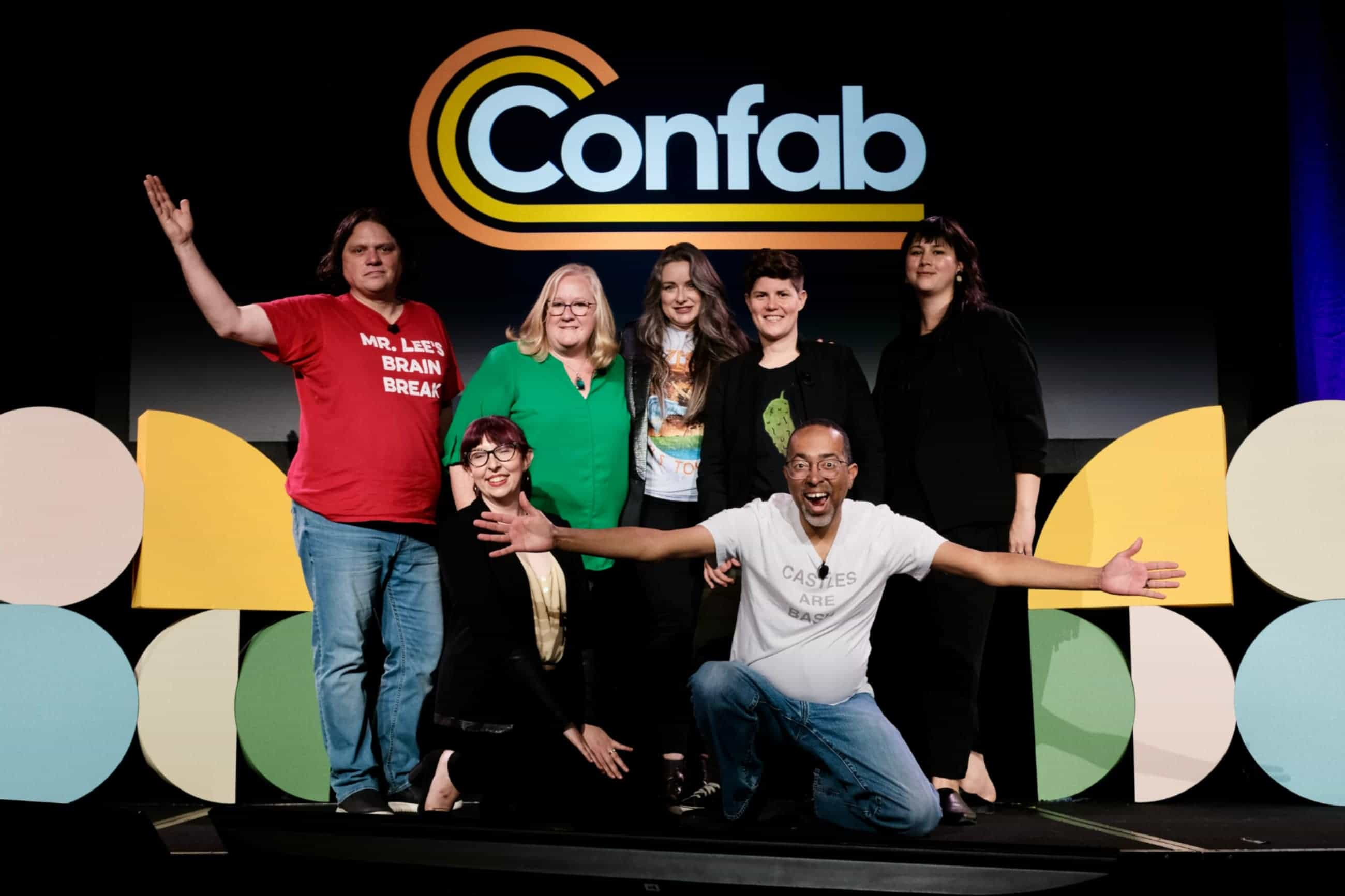 Several people posing for a group photo on stage. The Confab logo is hanging behind them.